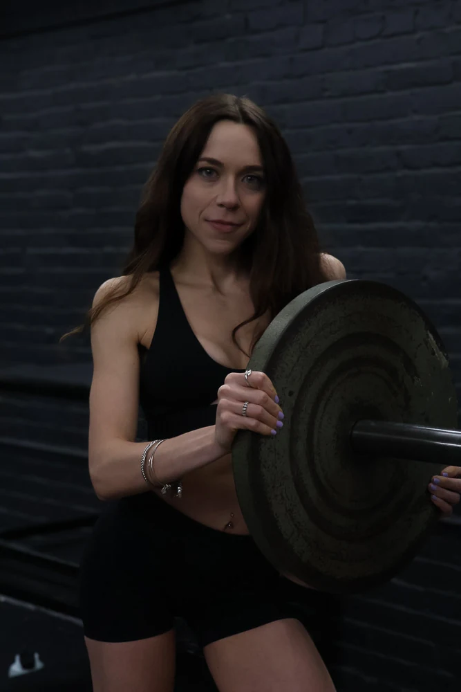 Jasmine beside a barbell and weight plate in the gym